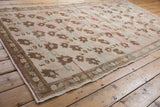 Distressed Oushak rug corner, showing bronze leaf border and worn blush, seafoam field.