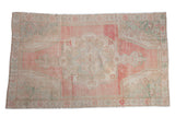 Distressed vintage Oushak rug with a central medallion, featuring an abrashed pink field and seafoam green accents.