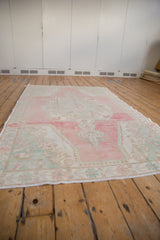 Low angle view of a vintage Oushak runner showing its abrashed pink field and overall distressed texture.
