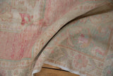 Soft folds of a distressed Oushak runner showing its worn texture in pink and seafoam.