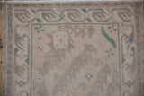 Distressed Oushak rug close-up showing worn beige, ivory, and green serrated leaf border and fringe.