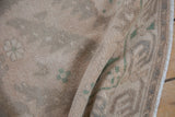 Vintage distressed Oushak rug detail, soft beige pile with muted dusty green motifs, even wear.