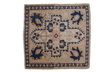 Distressed Oushak square rug with navy blue shield medallion, beige ground, and floral palmettes.
