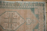 Distressed beige Oushak rug detail, showing deep seafoam geometric border and fringe.