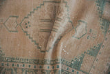 Distressed vintage Oushak rug pile with geometric seafoam patterns and visible foundation.