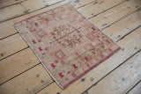 Angled view of a vintage Oushak square rug, showcasing distressed raspberry and ivory geometric patterns.