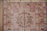 Distressed Oushak rug showing geometric stepped medallion with faint foundation, pale raspberry red.