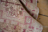 Rolled vintage Oushak rug close-up, revealing even wear and geometric patterns in raspberry and ivory.