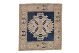 Distressed Oushak square rug with dark blue serrated medallion and beige germinating plant motifs.