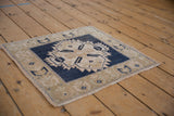 Distressed Oushak square rug with serrated blue medallion on an abrashed tan ground.