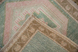 Distressed vintage Oushak rug corner showing seafoam green, pale blush pattern, woven selvage.