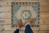 Distressed Oushak rug corner, seafoam green field, deep bronze floral geometric border, even wear.