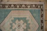 Distressed Oushak corner: seafoam green, beige geometric, deep bronze vine border, even wear.