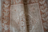 Distressed Oushak rug's worn pile texture in soft ivory and copper bronze tones.