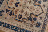 Distressed vintage Oushak rug close-up: beige field, navy meandering vine border, and floral motifs.
