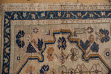 Distressed vintage Oushak rug with beige field, navy blue meandering vine border, and even wear.
