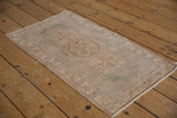 Distressed Oushak rug border featuring geometric vine and floral motifs in beige and seafoam green.