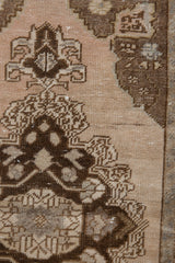 Distressed Oushak rug detail: chocolate brown corner spandrel on an antique ivory abrashed field.