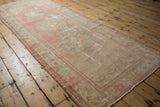 Distressed pink and beige Oushak runner side, revealing floral patterns and areas of exposed foundation.