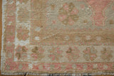 Fringed corner of vintage distressed Oushak runner with soft rose and beige vine pattern.