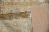 Distressed Oushak rug corner revealing worn beige pile and dusty rose foundation.