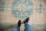 Distressed vintage Oushak carpet showing roundel medallion with blue floral vinery on beige.