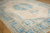 Distressed vintage Oushak rug corner with sky blue floral book cover spandrel on beige field.