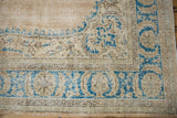 Distressed Oushak rug corner: blue curvilinear vinery, beige book cover spandrel, and worn patterned borders.