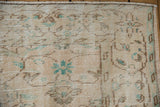 Distressed Oushak rug corner with worn pile texture and faded beige, green floral vinery.