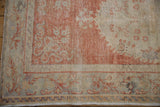Vintage distressed Oushak rug corner with pale cinnabar vine border and visible foundation wear.