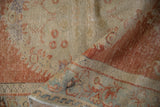 Distressed vintage Oushak rug folded, highlighting border's faded cinnabar red and pale blue design.