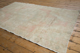 A distressed Oushak rug corner showcasing soft blush, ivory, sea foam green, and even wear.