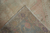Folded corner of vintage distressed Oushak rug, revealing faded pile and intricate slate, blush foundation.