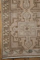 Corner of distressed Oushak rug, showing geometric patterns, worn ivory pile, and fringe.