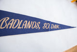 Tan script reading 'Badlands, So. Dak.' on the vintage blue felt pennant.