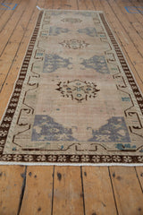 End of vintage Oushak runner with distressed pile, coffee brown border, and muted geometric patterns.
