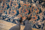 Feet on distressed vintage Oushak runner, highlighting indigo and terracotta geometric motifs.