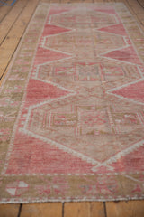 Distressed vintage Oushak runner showing worn pink, beige geometric floral motifs and side selvage.