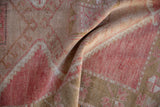 Distressed Oushak rug pile showcasing geometric floral patterns in dusty raspberry red and beige.