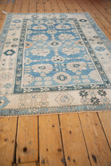 Distressed pile of a vintage Oushak rug, showing intricate blue and ivory border patterns.