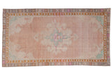 Distressed vintage Kars carpet with a large scrolling medallion on a dusty blush field with mint green accents.