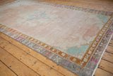 Angled view of a Kars carpet's faded blush field and detailed pastel-colored border.