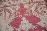 Pale cochineal red and ivory stylized floral motifs on the distressed Oushak rug pile.