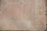 Detail of distressed Oushak rug, worn pale pink and beige pile with visible fringe.