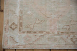 Texture of distressed Oushak rug corner with faded ivory, blush, brown geometric motifs.