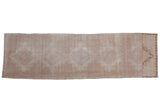 Vintage distressed Oushak runner with a repeating geometric medallion in muted, even-wearing tones of beige and sand.