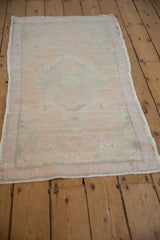 Distressed vintage Oushak rug with a soft, faded pastel pattern viewed from an angle.