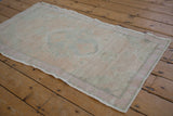 Angled view of a vintage Oushak rug highlighting its time-softened pastel green and pink hues.