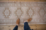 Distressed vintage Oushak runner featuring repeating geometric gul design in beige tones.