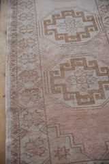 Distressed Oushak rug close-up: worn beige pile, visible foundation, coffee geometric patterns.